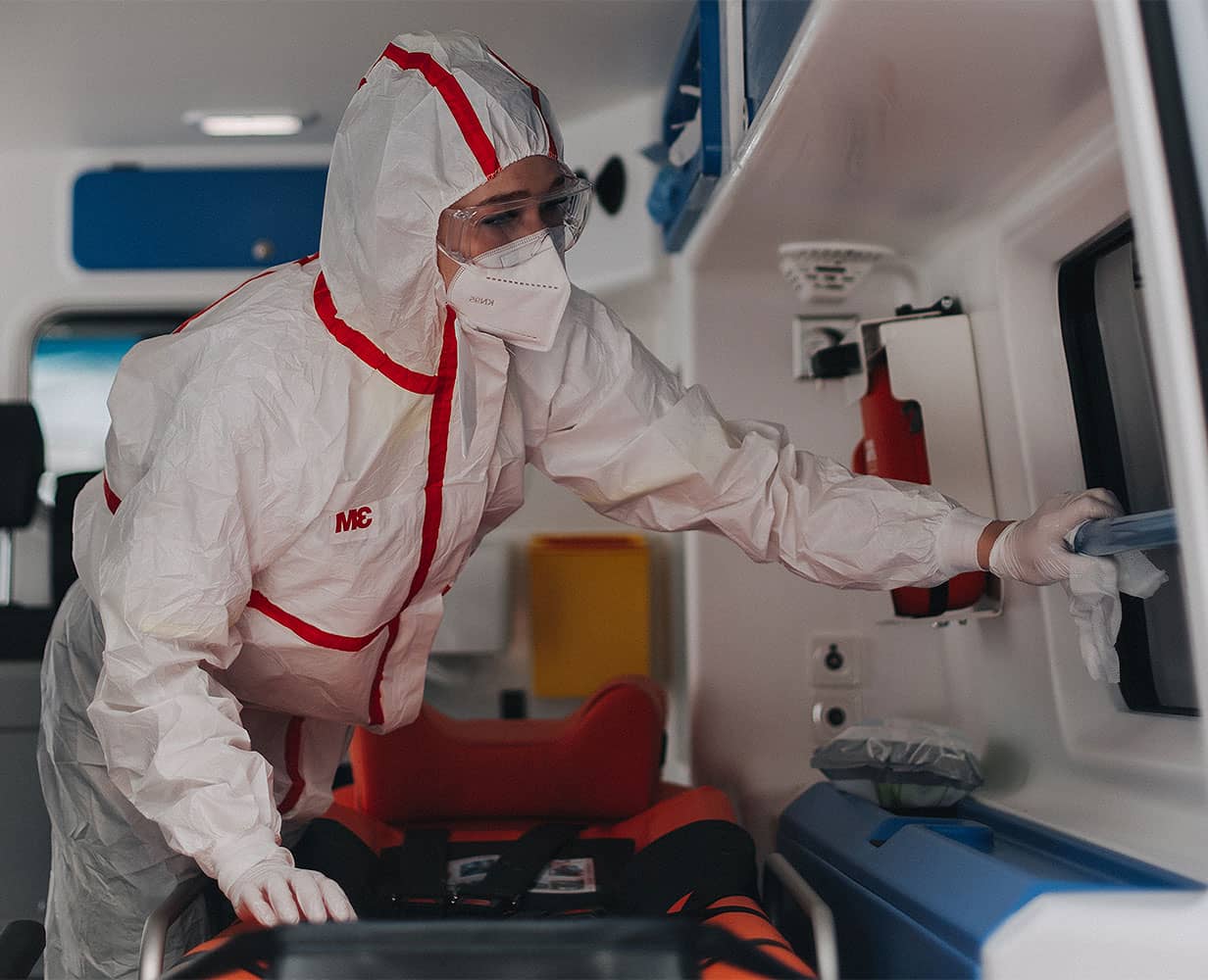 Junge Sanitäterin in Schutzkleidung reinigt Innenraum eines Krankenwagens